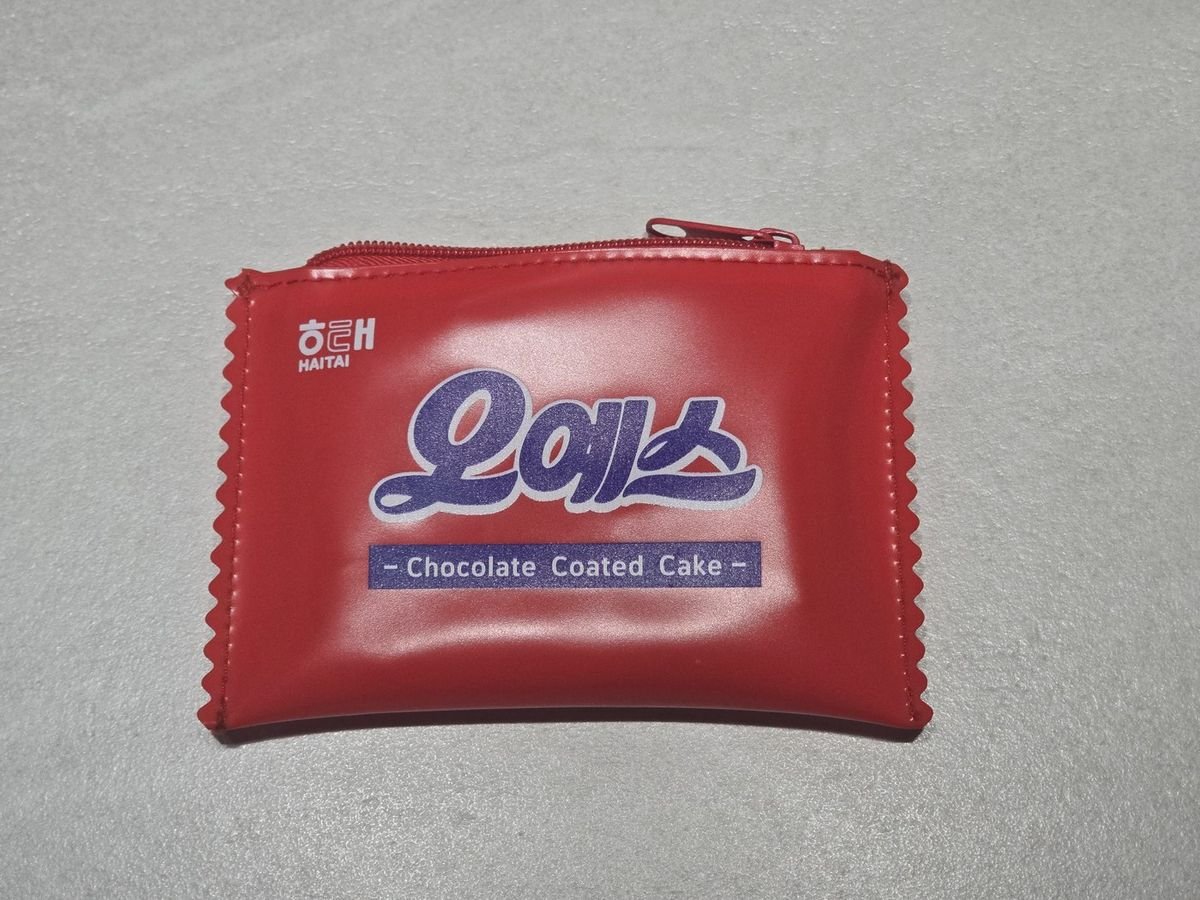해태 오예스 포장지 모양을 그대로 옮긴 빨간 지퍼 파우치. HAITAI 로고와 오예스, Chocolate Coated Cake 글자가 인쇄되어 있다